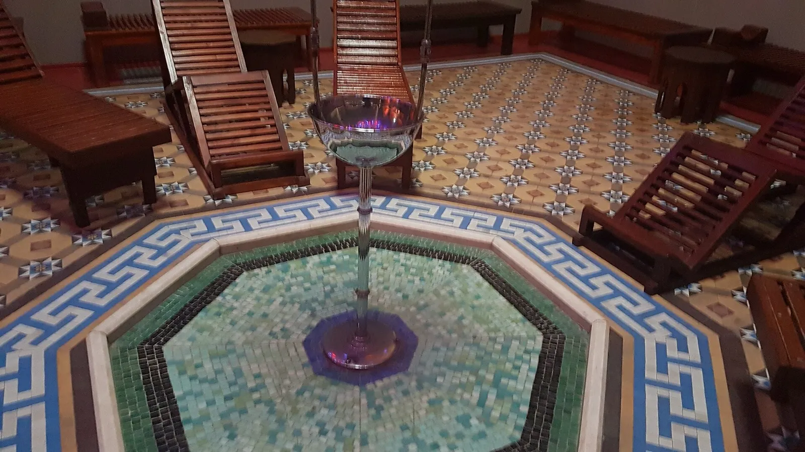 Sala do banho turco do Arlington Baths Club, com piso de ladrilhos, fonte octogonal de mosaico e espreguiçadeiras de madeira