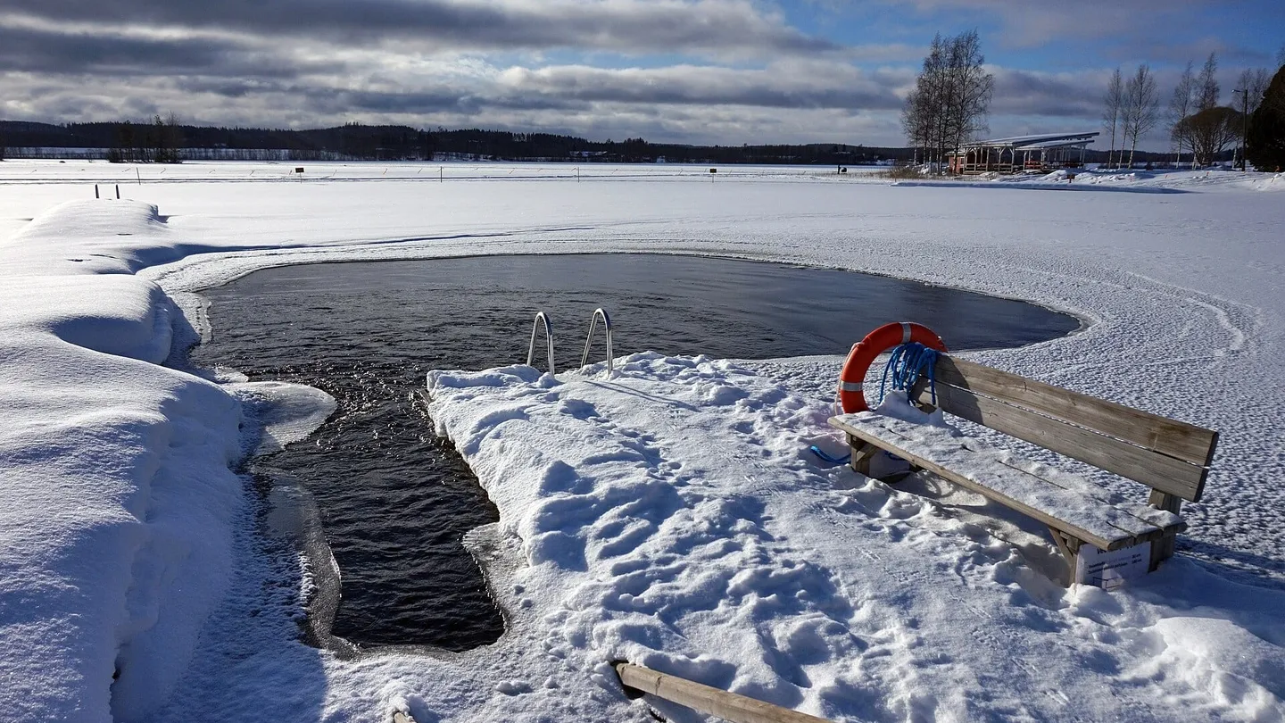 Buraco no gelo para banho de inverno num lago congelado em Peurunka, na Finlândia, com escada, boia e banco na neve