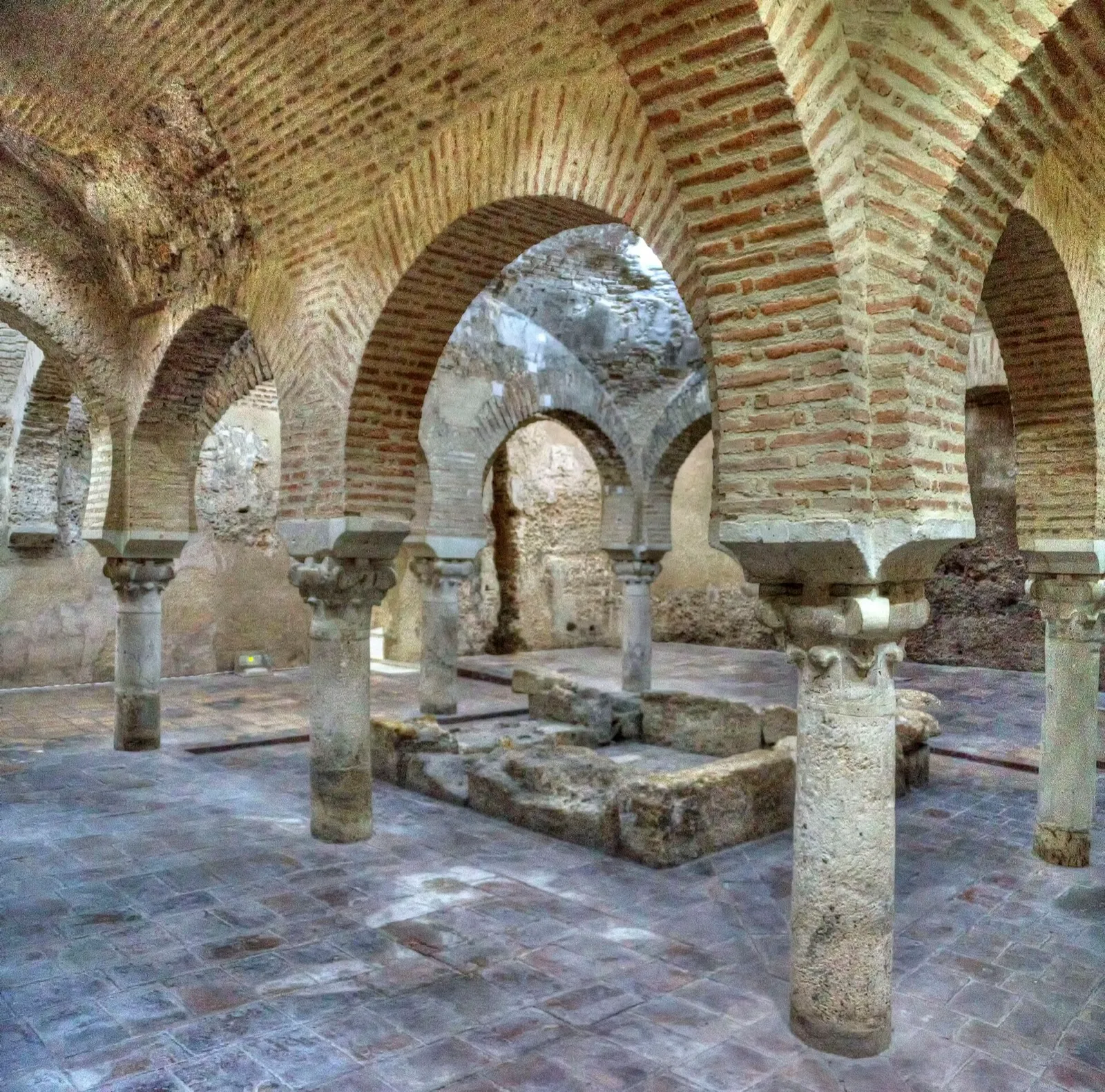 Sala central dos banhos árabes de Jaén, com arcos de ferradura de tijolo sobre colunas de pedra e uma pia no centro