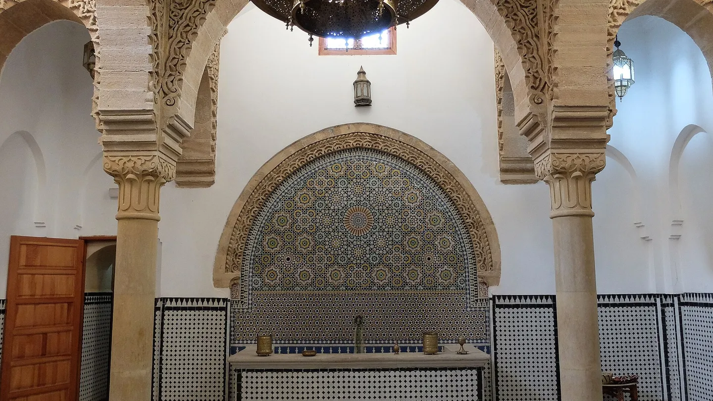 Salão de recepção do Hammam Saffarin, em Fez, com arcos de estuque entalhado, fonte de parede em mosaico e piso xadrez