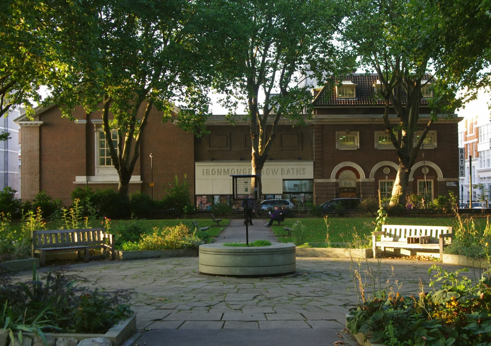 Fachada de tijolo dos Ironmonger Row Baths vista do jardim atrás da igreja de St Luke, com árvores e bancos