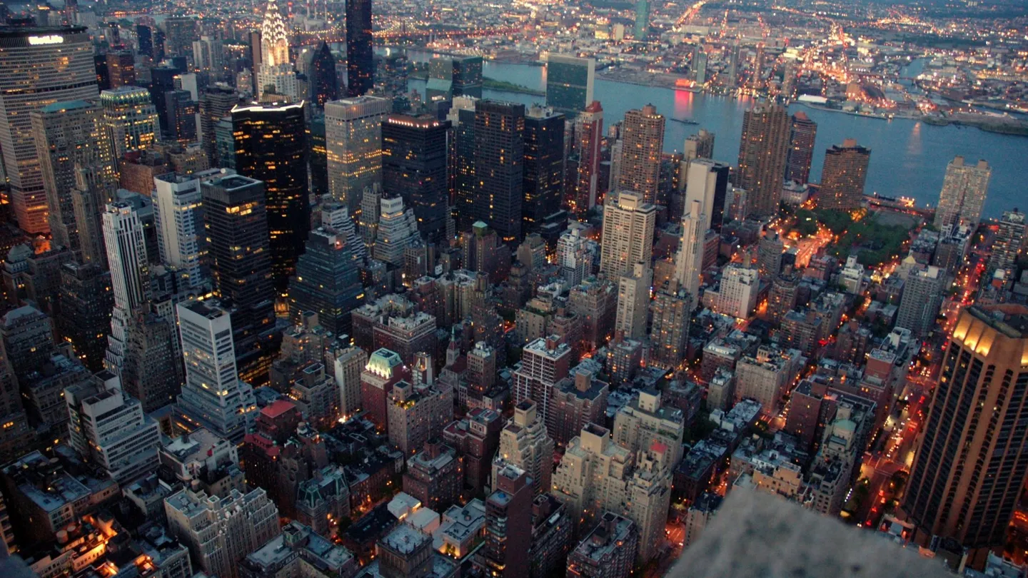 Manhattan vista do alto ao entardecer, com os prédios de Midtown acesos e o East River ao fundo