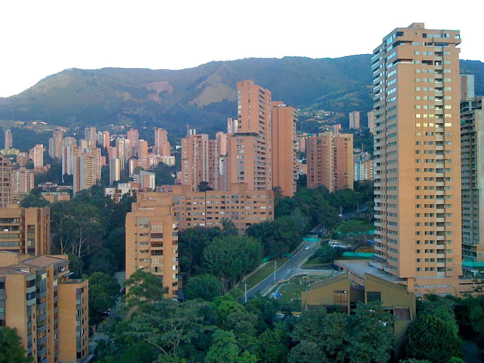 Vista de El Poblado, em Medellín, com prédios de tijolo entre árvores e as montanhas ao fundo