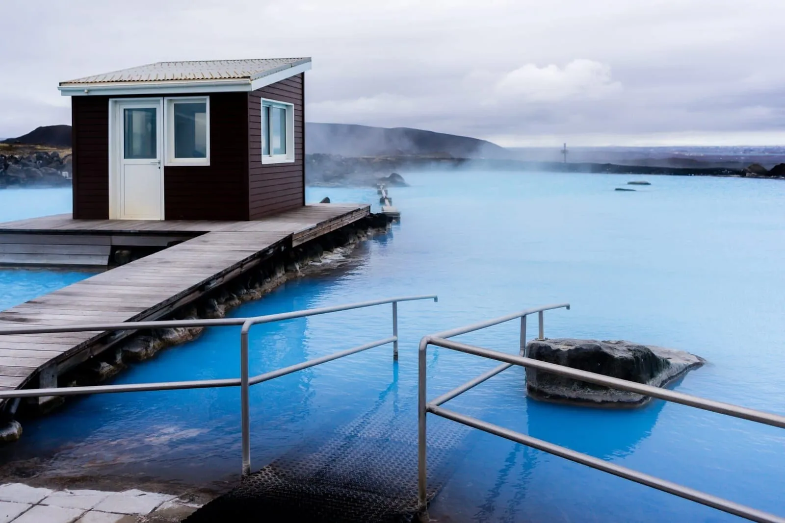 Lagoa azul-turquesa dos Mývatn Nature Baths, com deque de madeira, corrimão e vapor sobre a água