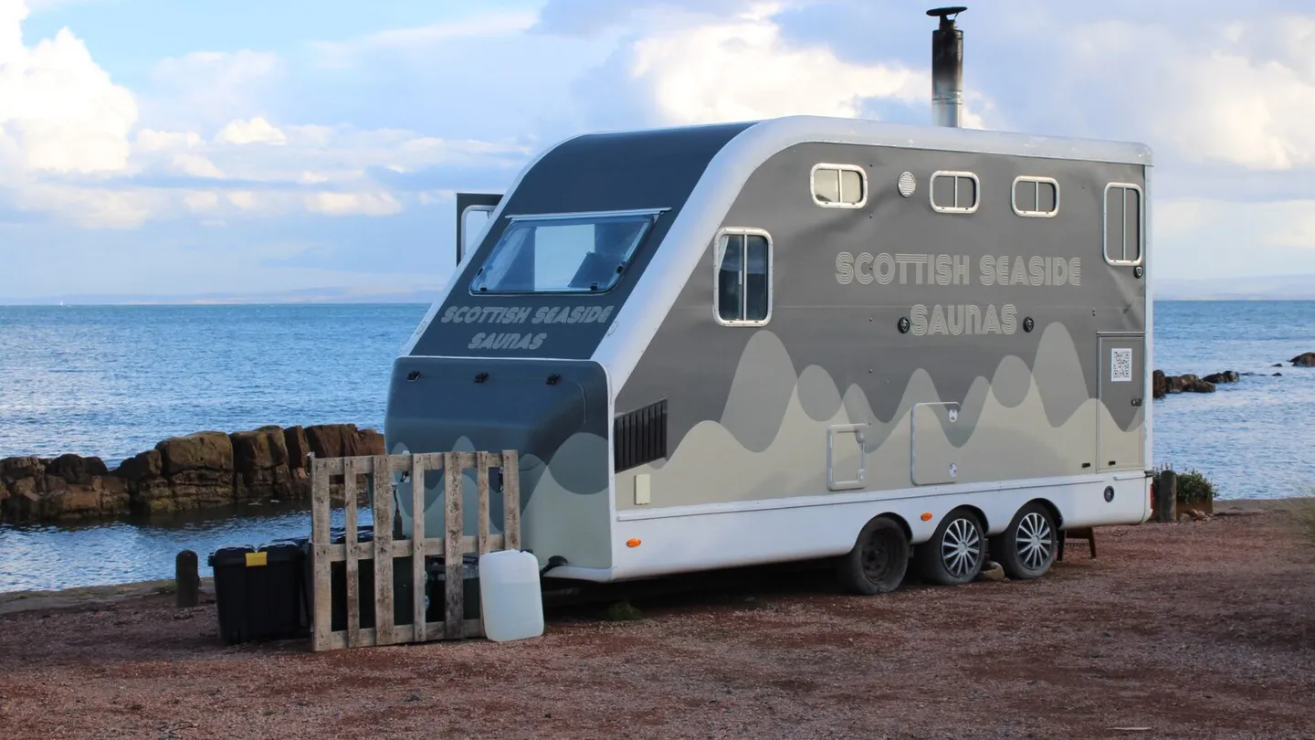 Sauna montada num reboque cinza da Scottish Seaside Saunas, estacionada sobre o cascalho à beira do mar em Cellardyke, em Fife