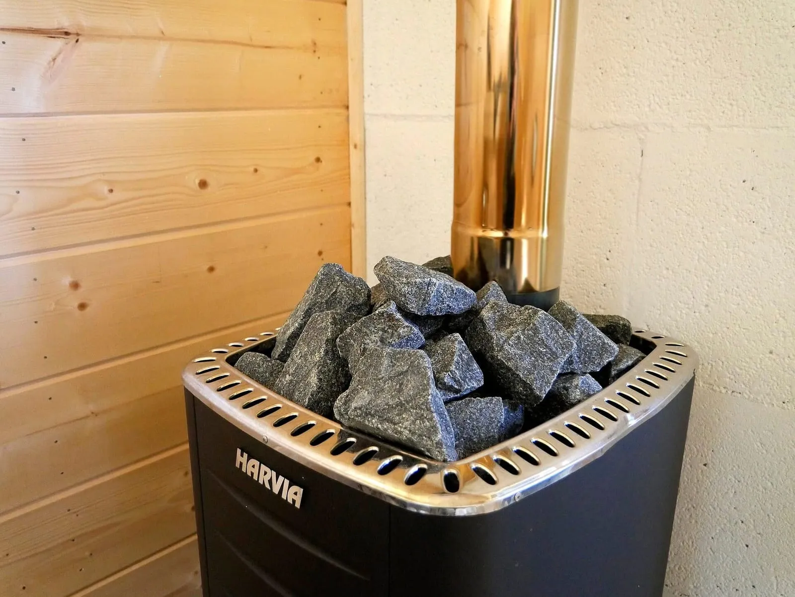 Aquecedor de sauna elétrico preto com pedras no topo, num canto de sauna de madeira clara