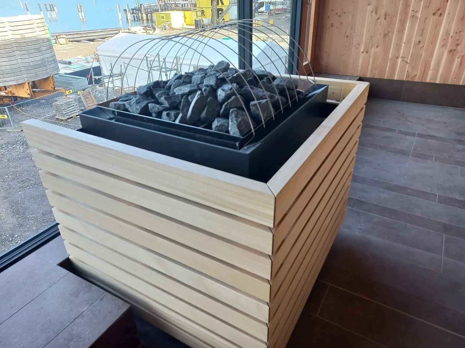 Aquecedor de sauna com pedras, envolto em ripas de madeira, numa sauna ainda em obra em Bregenz