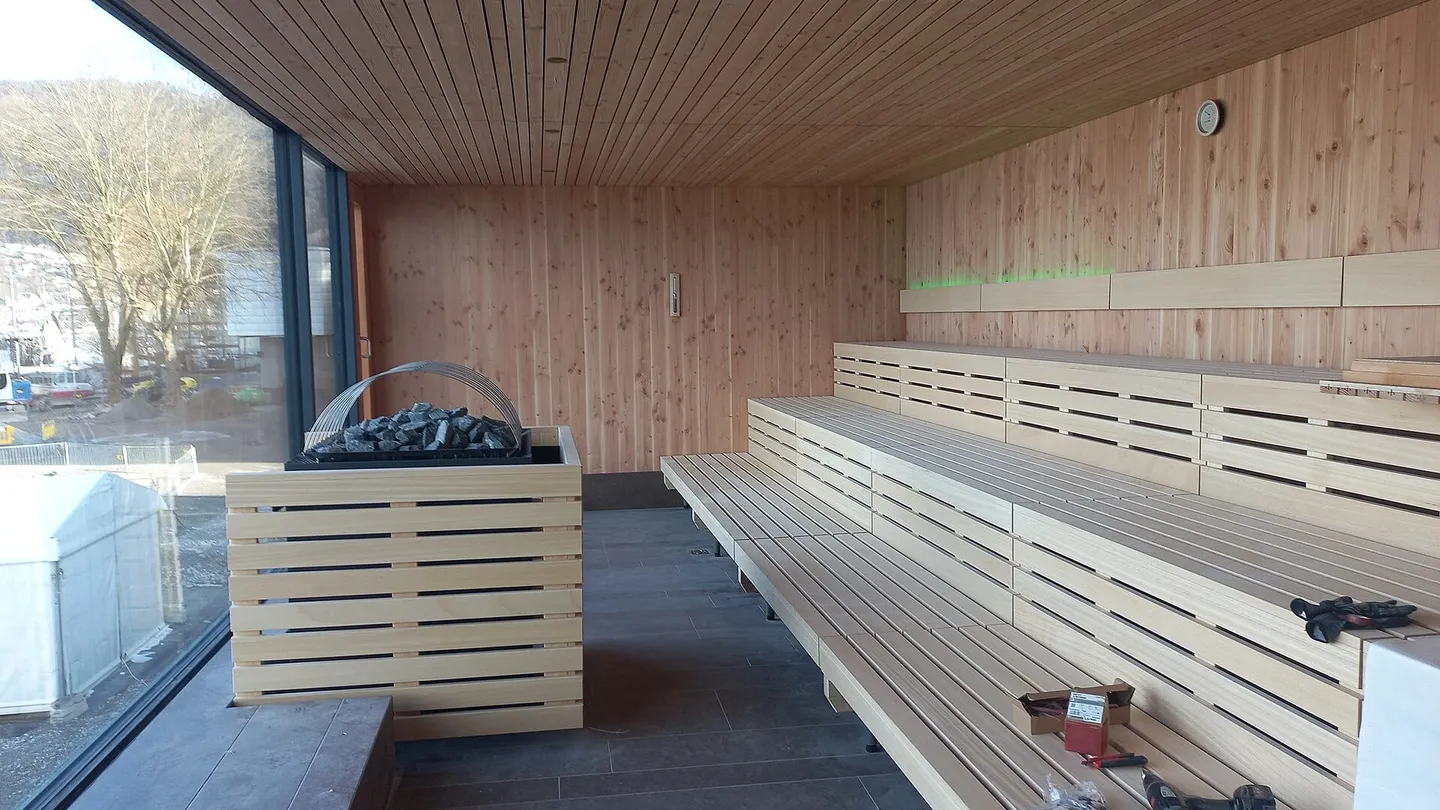 Sauna em construção no Seebad de Bregenz, na Áustria, com bancos de madeira clara, aquecedor e janela para o lago