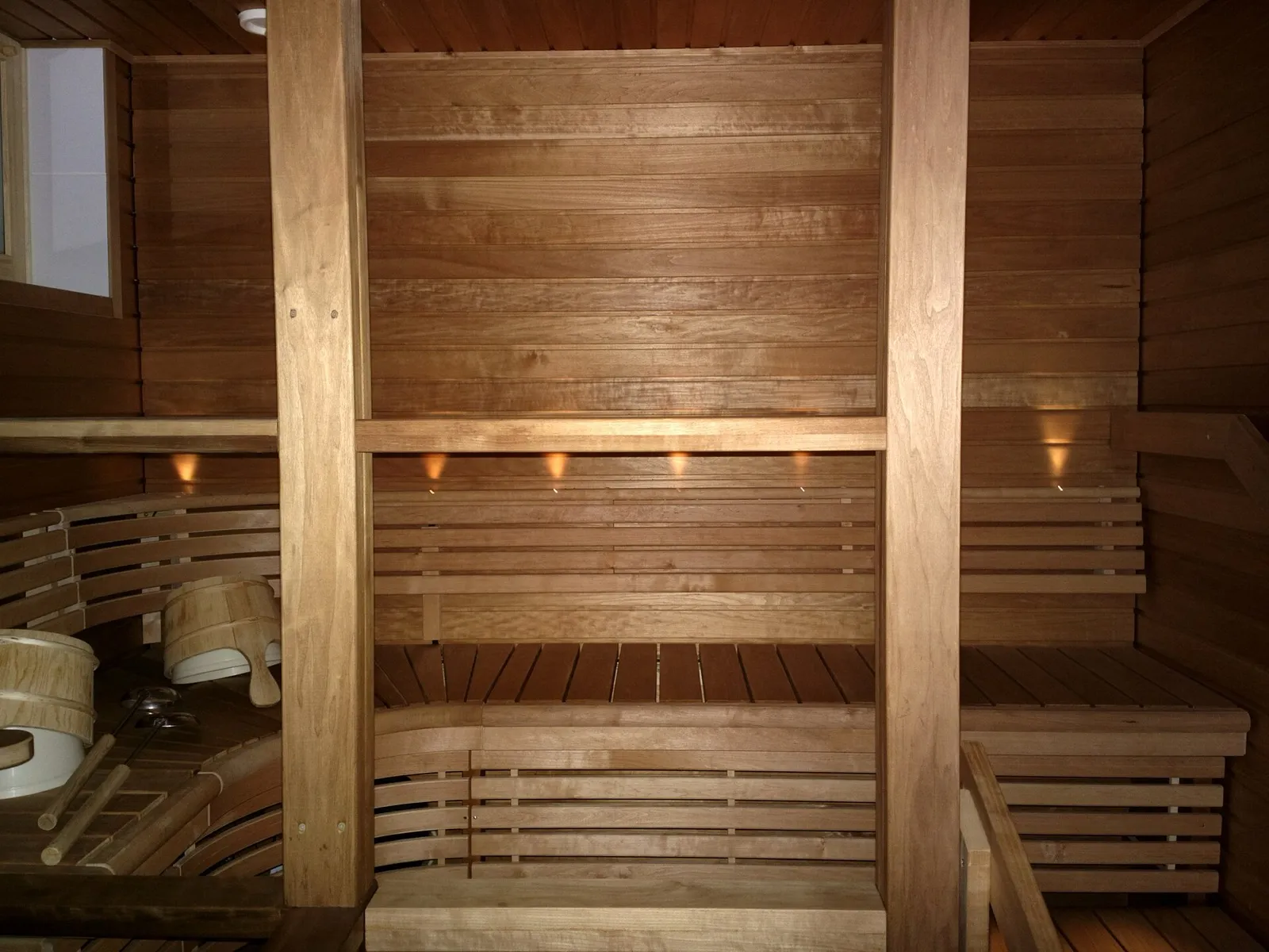 Interior de uma sauna finlandesa com bancadas de ripas de madeira em dois níveis, encosto, balde e concha de madeira