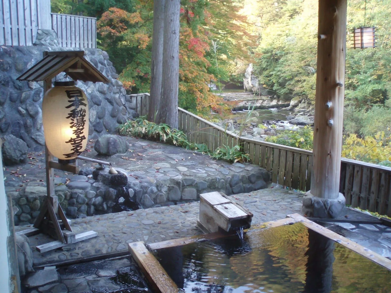 Banho de pedra ao ar livre no Takanoyu Onsen, em Akita, entre árvores e uma lanterna de madeira