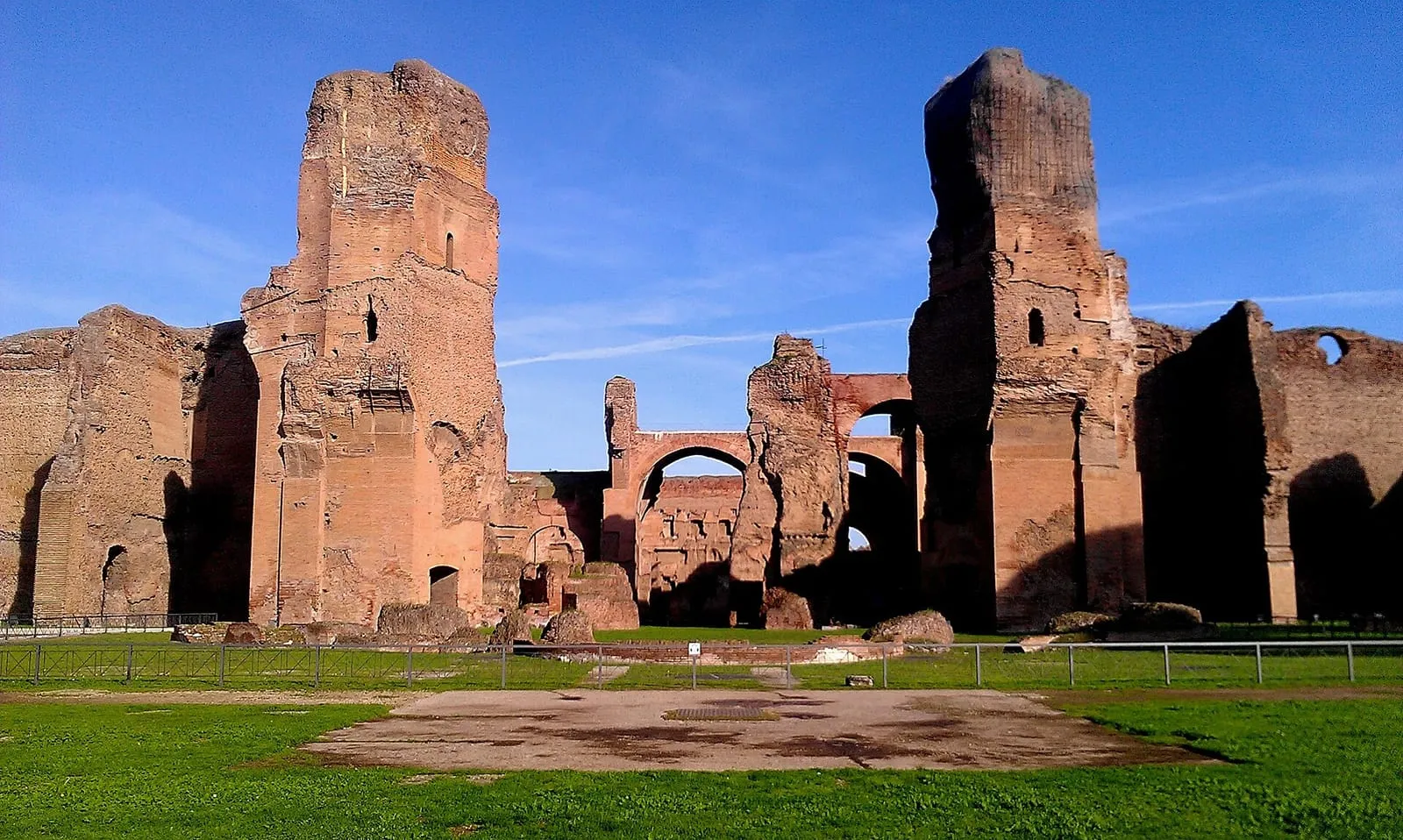 Ruínas de tijolo das Termas de Caracala, em Roma, com paredes altas e arcos vistos do gramado em direção ao caldário